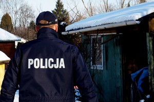 policjant odwrócony plecami, w tle altanka ogrodowa