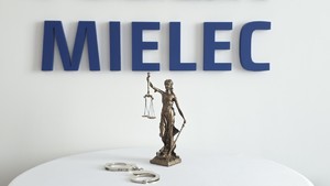 Zdjęcie figury Temidy na tle napisu MIELEC, obok figurki na stoliku leżą kajdanki policyjne
