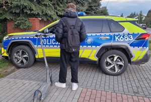 radiowóz, a przy nim kierujący hulajnogą